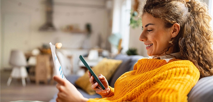 Woman in yellow sweater paying bills on her phone