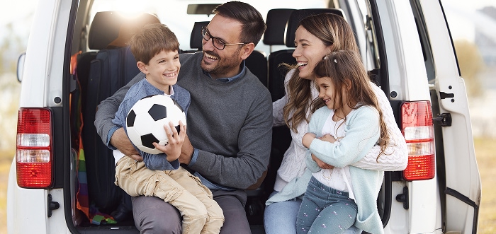 Family with two kids sitting in the back of their car with a soccer ball