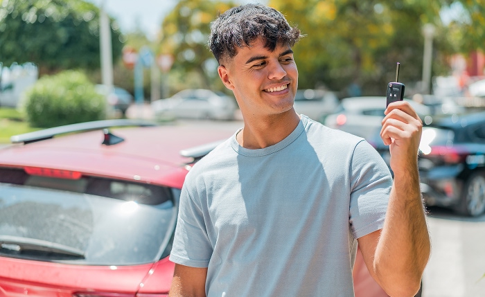 A young man with car insurance holding up the key to his car