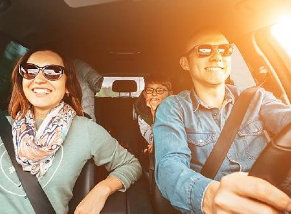 Photo shows a family inside their car smiling.